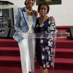 Helen Cummings-Henry at the pulpit with guest wearing blue jacket and white pants