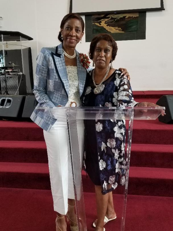 Helen Cummings-Henry at the pulpit with guest wearing blue jacket and white pants